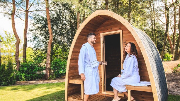 A wooden pod-shaped structure with a door, a bench inside, and a person standing outside. - Modern Holiday Home With Infrared Sauna (Slagharen)