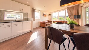 A modern kitchen with white cabinets, a wooden dining table, and a brown leather sofa. - Modern Holiday Home With Infrared Sauna (Slagharen)