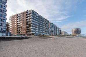Ein Hochhaus-Hotel mit mehreren Etagen, ein Strand im Vordergrund und ein auffälliges, kreisförmiges Gebäude im Hintergrund.
