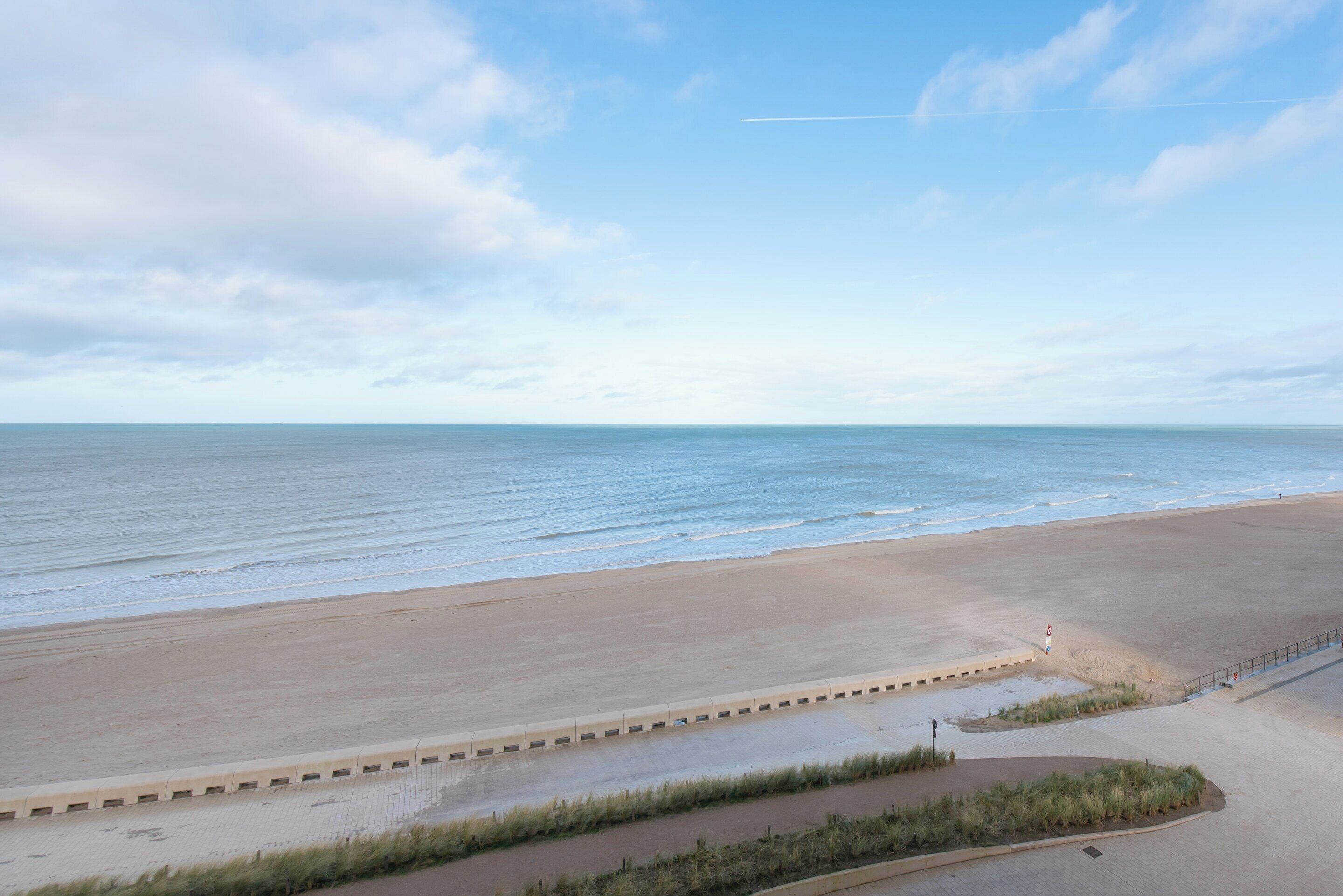 Een strand met een verharde promenade, een uitkijktoren van de badmeester en een heldere lucht.