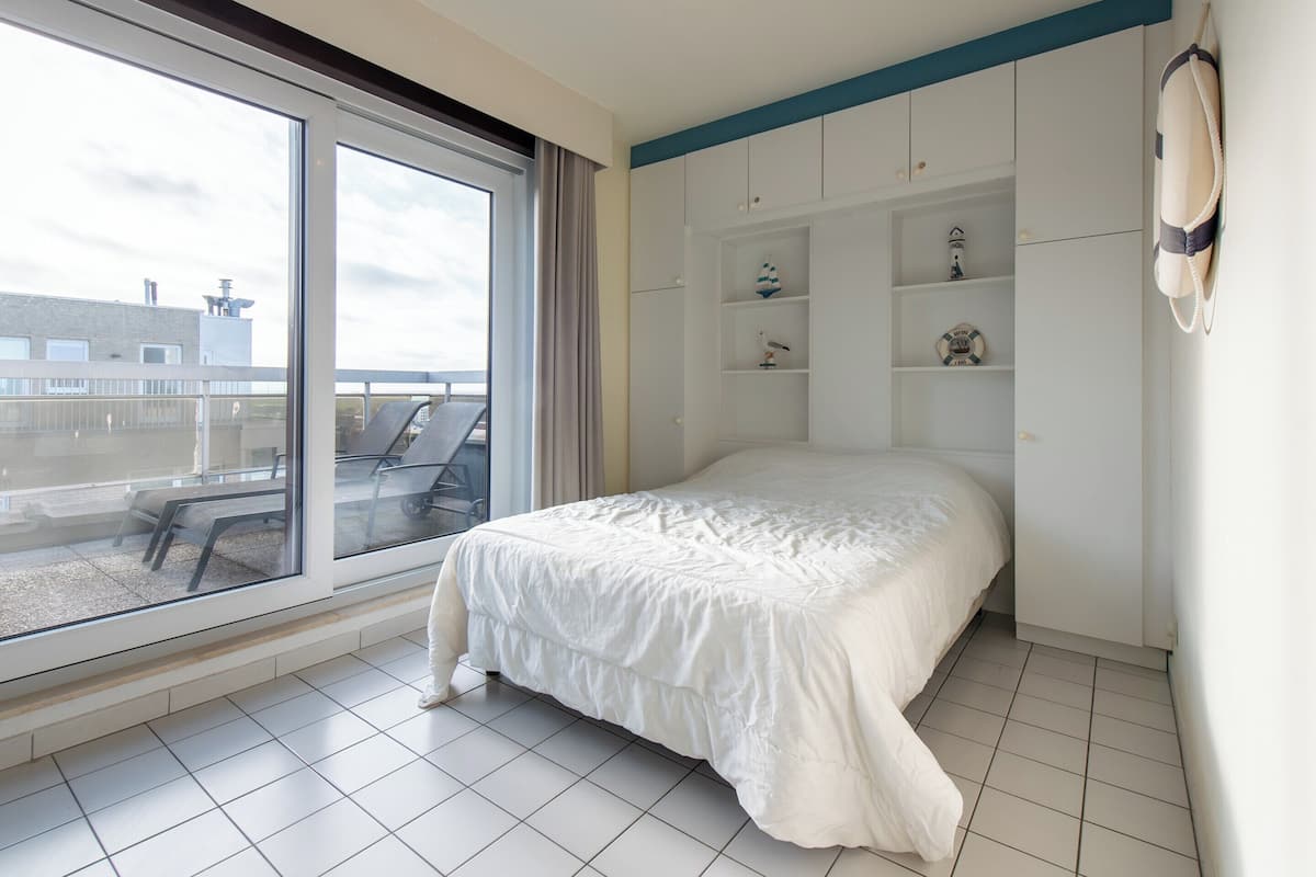 Ein Schlafzimmer mit großem Fenster, einem Bett und integrierten Regalen mit Dekoration.