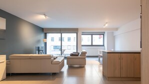 A modern living room with a sofa, a smaller seating area, and a kitchen area with wooden cabinets. - Apartment in Ostend Near the Seawall (Ostend)