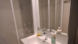 Un baño con lavamanos blanco, un espejo y cabina de ducha con paredes de vidrio.