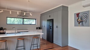 Une cuisine moderne dotée d’un grand îlot central, de tabourets de bar, d’un réfrigérateur et d’une fenêtre donnant sur les arbres.