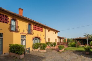 A yellow building with a balcony, potted plants, and a paved courtyard. - Mansion With Pool and Play Area (Castelfranco Piandisco)