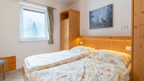 Makuuhuoneessa on sänky, ikkunassa verhot, puinen vaatekaappi ja seinällä taulu.
