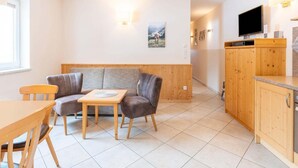 Moderni hotellihuone, jossa on sohva, pieni pöytä, televisio ja puiset kaapit.