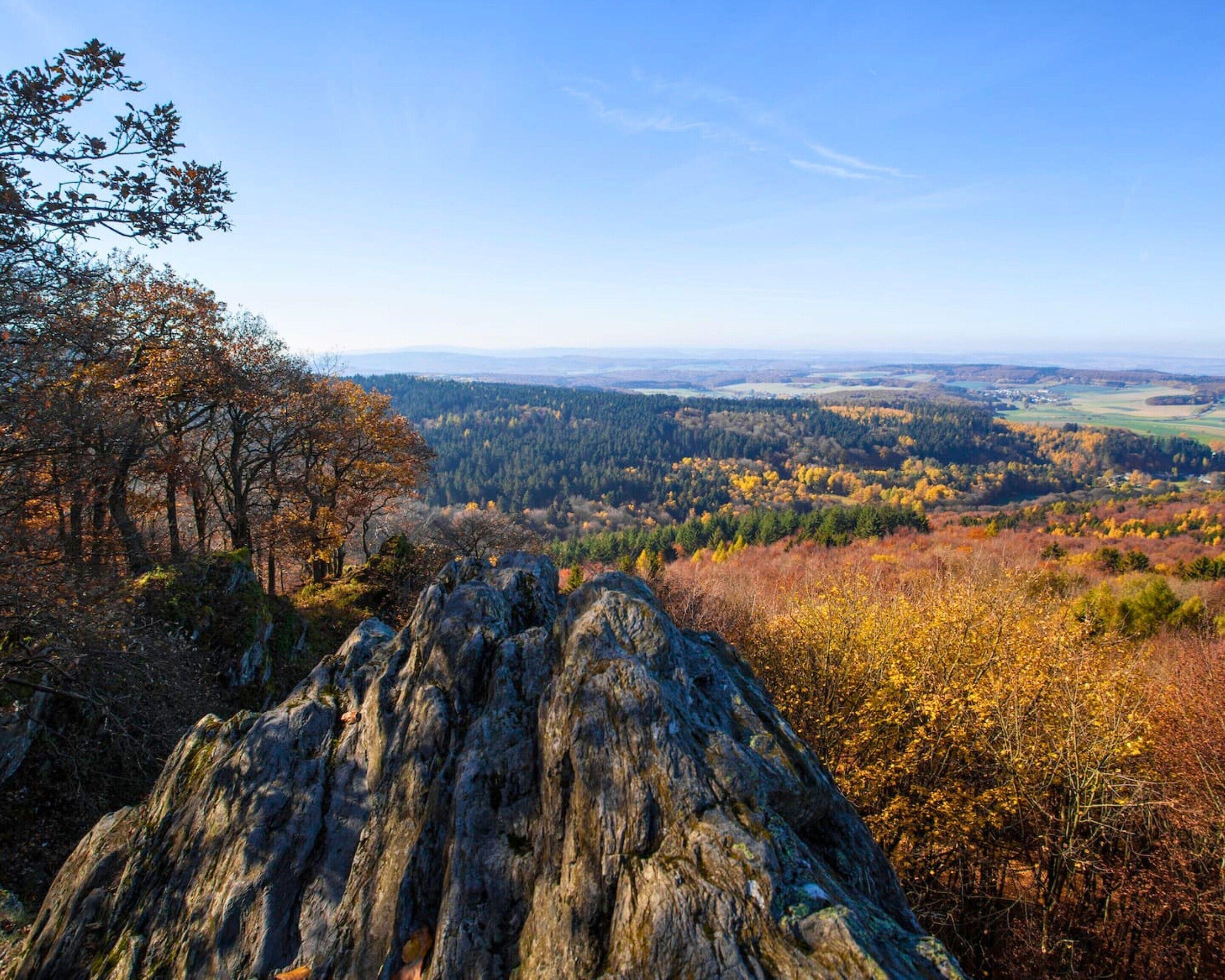 A rocky outcrop with a view of a forested valley and distant hills.