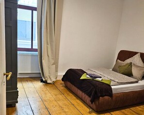 A bedroom with a wooden floor, a bed with multiple pillows, a window with curtains, and a radiator. - Modern Suite in the Taunus (Bad Camberg)