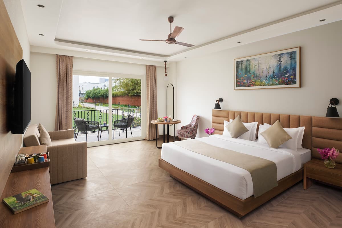 Hotelkamer met een groot bed, een flatscreen televisie, een plafondventilator, een schilderij en een balkon met buitenmeubilair.