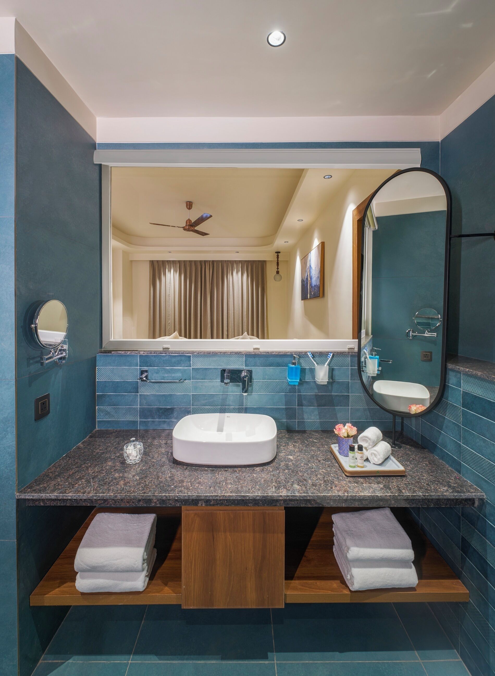 A modern bathroom with a large mirror, dual sinks, and a ceiling fan.