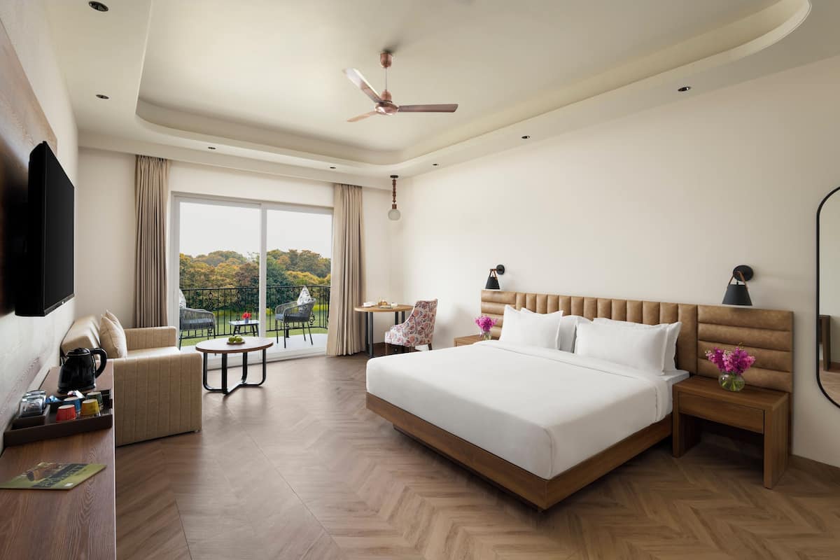 Hotelkamer met een groot bed, een flatscreen televisie, een plafondventilator, een balkon met uitzicht en een zithoek met een tafel en stoelen.