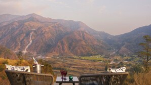 A table with a bottle and glasses, overlooking a mountainous landscape. - Treat Imperial Jim Corbett (Ramnagar)