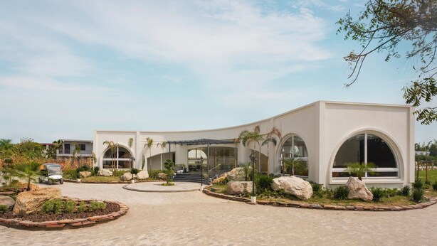A modern building with a curved facade, large arched windows, and a landscaped driveway with rocks and plants. - Treat Imperial Jim Corbett (Ramnagar)