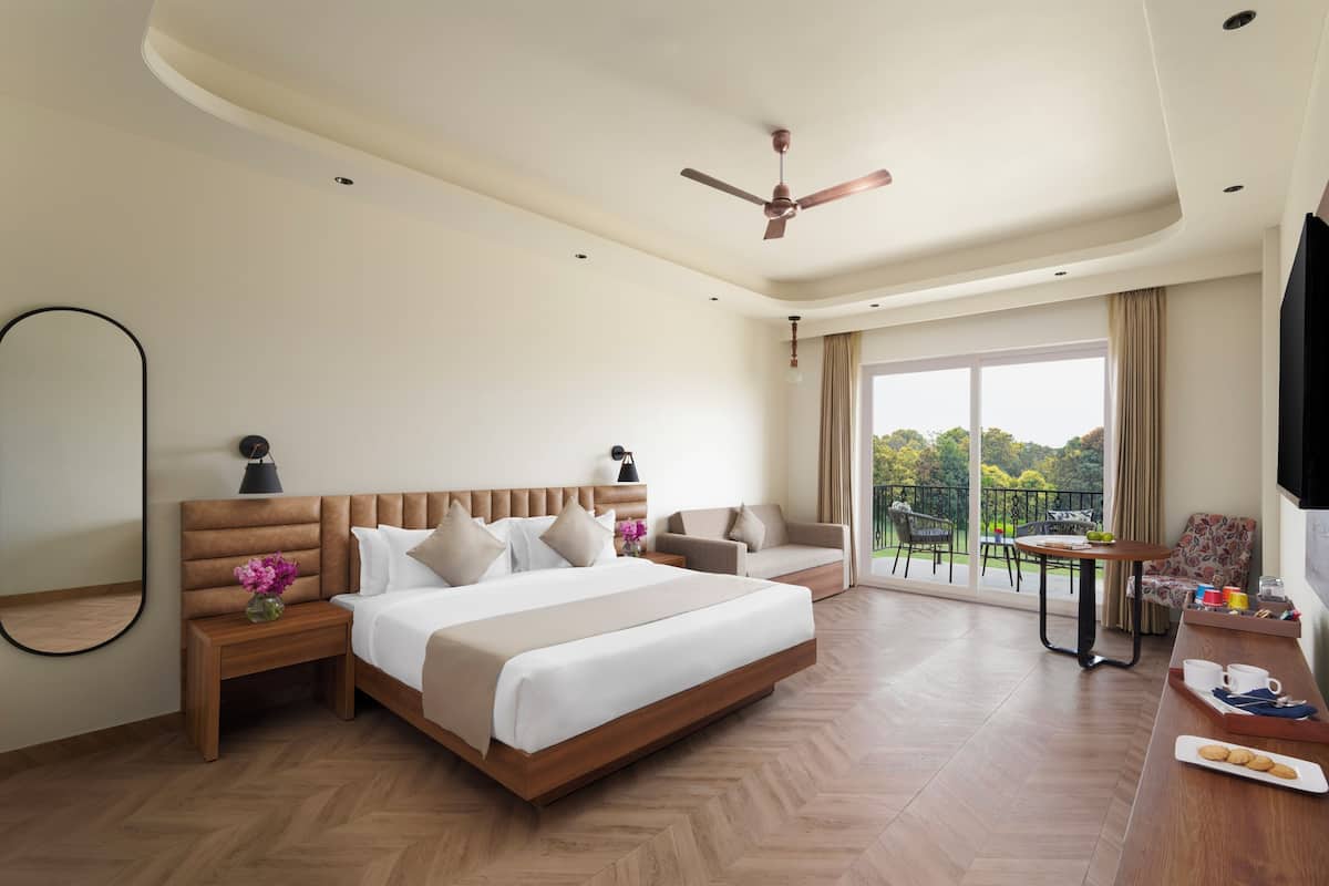 Hotelkamer met een groot bed, een zithoek met een tafel, een balkon met uitzicht en een plafondventilator.
