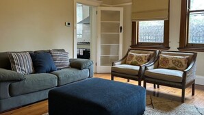 A living room with a sofa, ottoman, and two armchairs, a closet with a sliding door, and a window with blinds. - Heritage Charmer | Roomy and cosy | Central Orange (Orange)