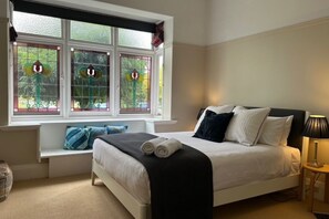 Un dormitorio con cama, almohadas, lámpara de noche y ventana con vidrieras.