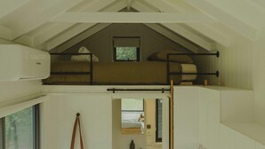Une chambre de style loft avec un lit superposé, une fenêtre et un appareil de climatisation.