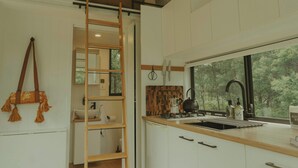Une cuisine moderne avec une échelle en bois, des armoires blanches, une fenêtre donnant sur les arbres et un sac suspendu.