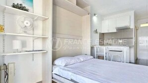 Um quarto com uma cama, uma escrivaninha e uma estante com um ventilador.