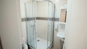 Ein modernes Badezimmer mit einer Glaskabine zur Dusche, weißen Fliesen und einem kleinen Waschbecken.