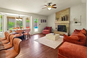 Ein Wohnzimmer mit Kamin, Deckenventilator und Essbereich mit Tisch und Stühlen.