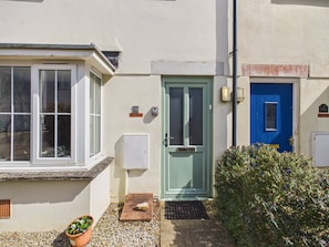 A house with a blue door, a white window, and a small garden area with a potted plant.
