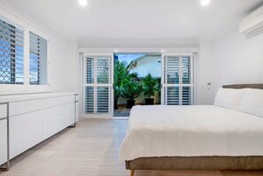A bedroom with a bed, a white wardrobe, and a sliding glass door leading to a balcony with plants. - Coastal Luxe - Diamond Beach 168 (Mermaid Beach)