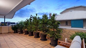 A rooftop terrace with potted plants, a white outdoor sofa, and a view of the city skyline. - Coastal Luxe - Diamond Beach 168 (Mermaid Beach)