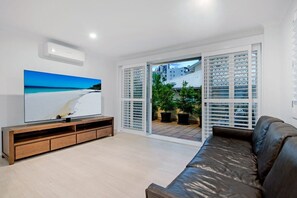 A living room with a TV, a sofa, and a sliding glass door leading to a balcony. - Coastal Luxe - Diamond Beach 168 (Mermaid Beach)