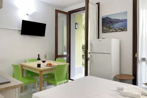A hotel room with a bed, a dining table with chairs, a TV mounted on the wall, a refrigerator, and a painting of a landscape. - Porto Letizia Mascagni 1, Porlezza, Italy (Porlezza)