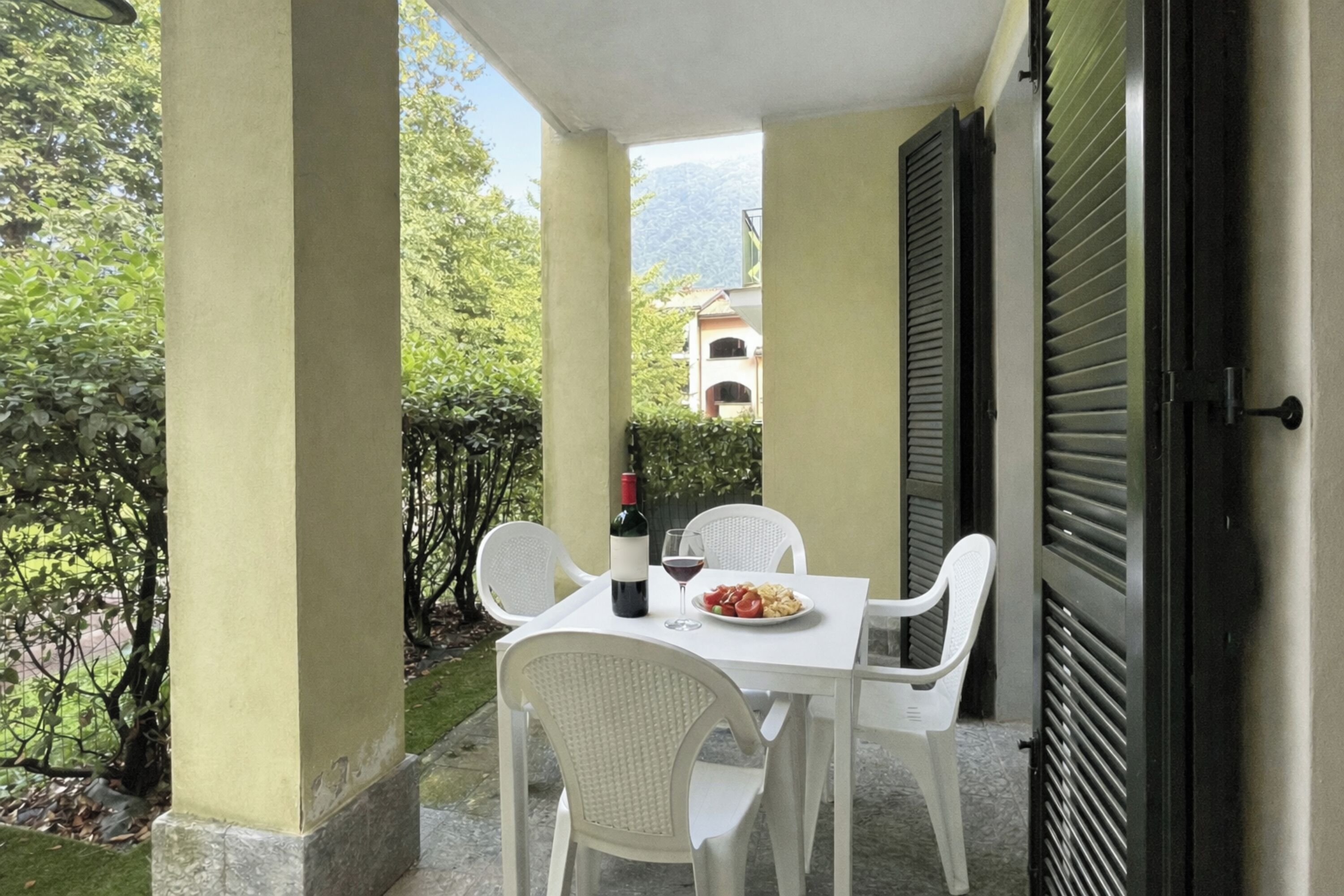 A balcony with a table, chairs, a bottle of wine, and a plate of food.