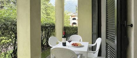 A balcony with a table, chairs, a bottle of wine, and a plate of food.