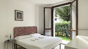 A bedroom with a bed, a bedside table, a chair, and a view of a garden through an open door. - Porto Letizia Mascagni 1, Porlezza, Italy (Porlezza)