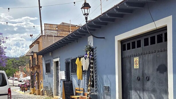 Une rue pavée avec une moto garée, un bâtiment bleu avec une porte de garage fermée, et un palmier en arrière-plan.