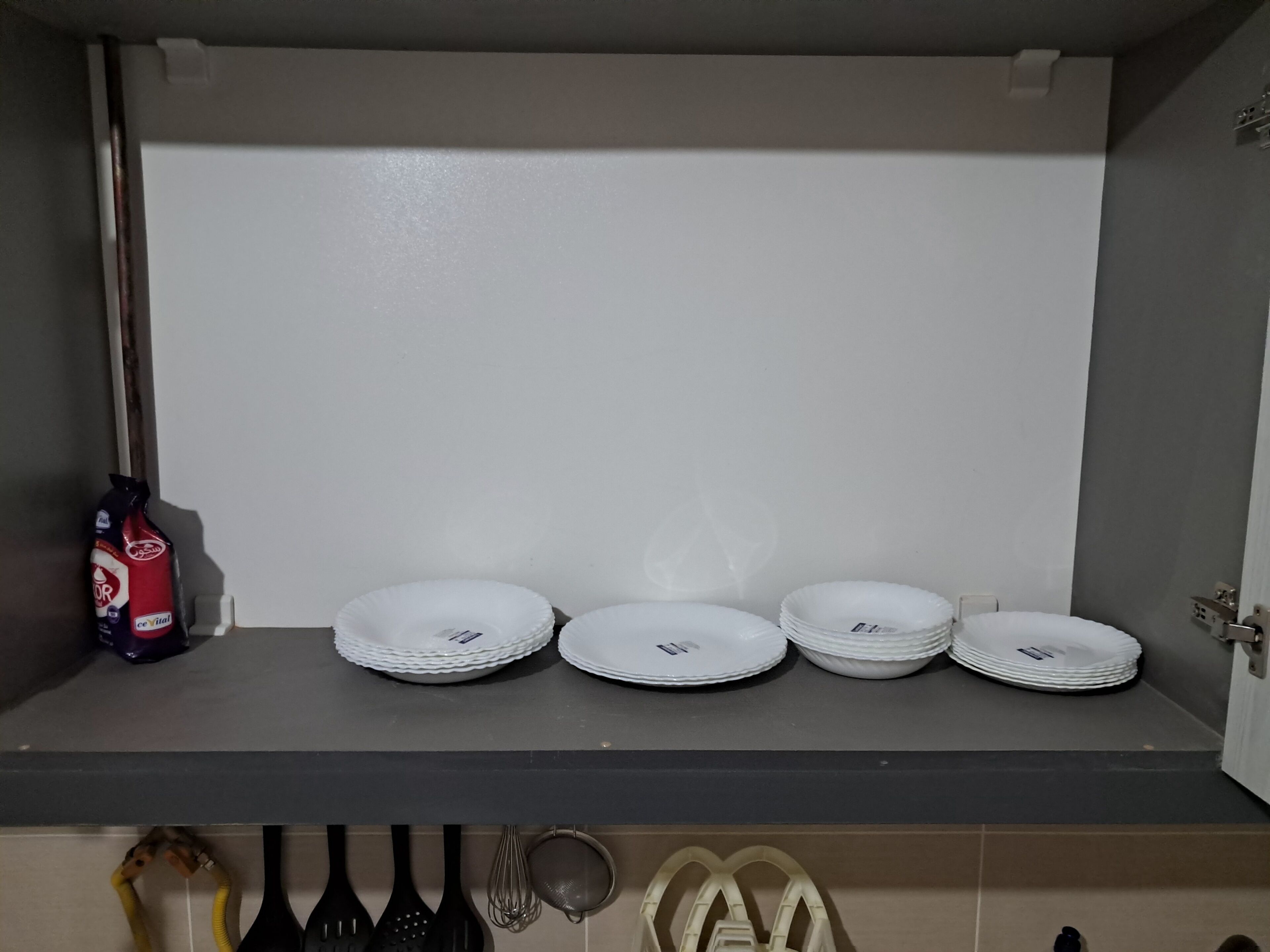 Un plan de travail de cuisine avec une pile d’assiettes blanches, une bouteille de détergent et des ustensiles de cuisine.