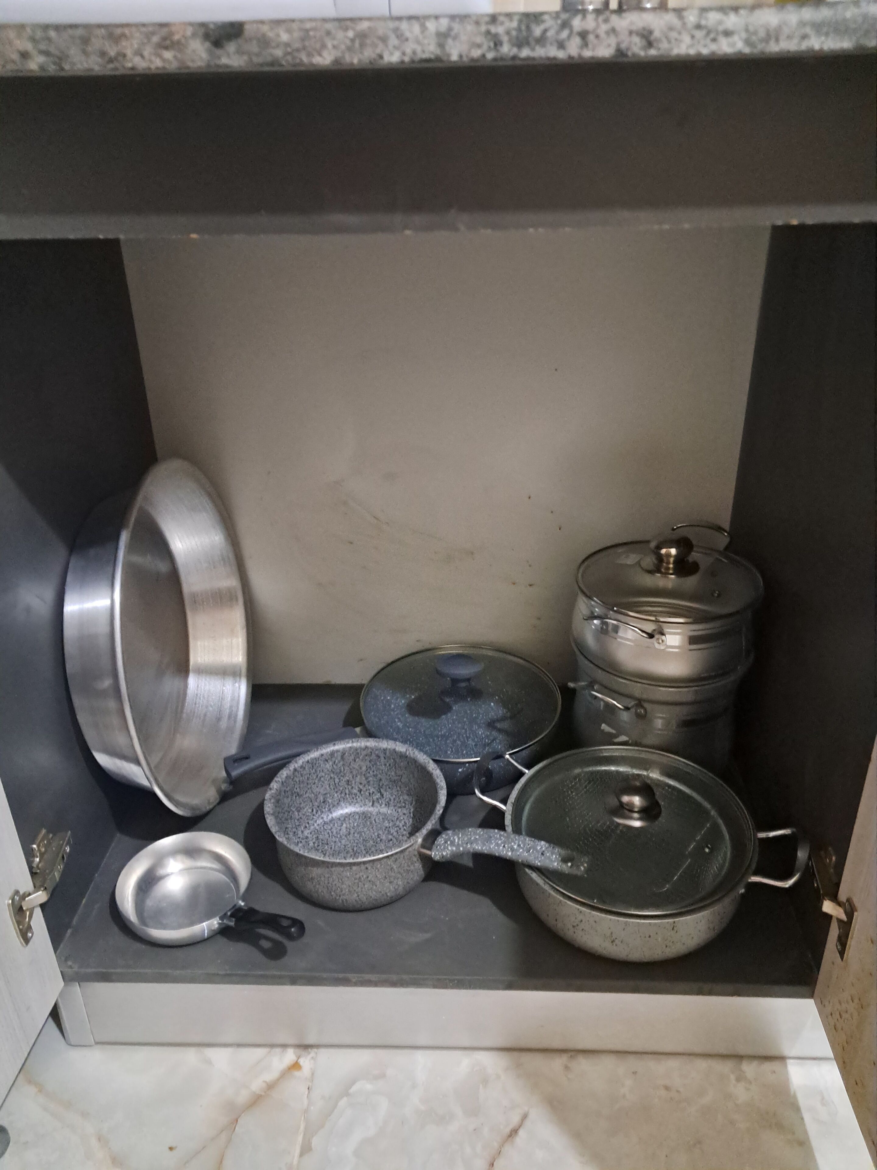 A kitchen cabinet with various cookware including pots, pans, and lids.