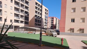 A multi-story residential building with balconies, a covered outdoor seating area, and a green lawn. - Rental per night apartment f4 standing equipped (Tlemcen)