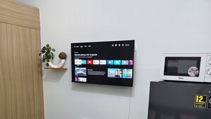 Eine moderne Küche mit Esstisch und Glasplatte, vier Stühlen, einem Kühlschrank, einer Mikrowelle und einem an der Wand befestigten Flachbildfernseher, der verschiedene Apps und Inhalte anzeigt.