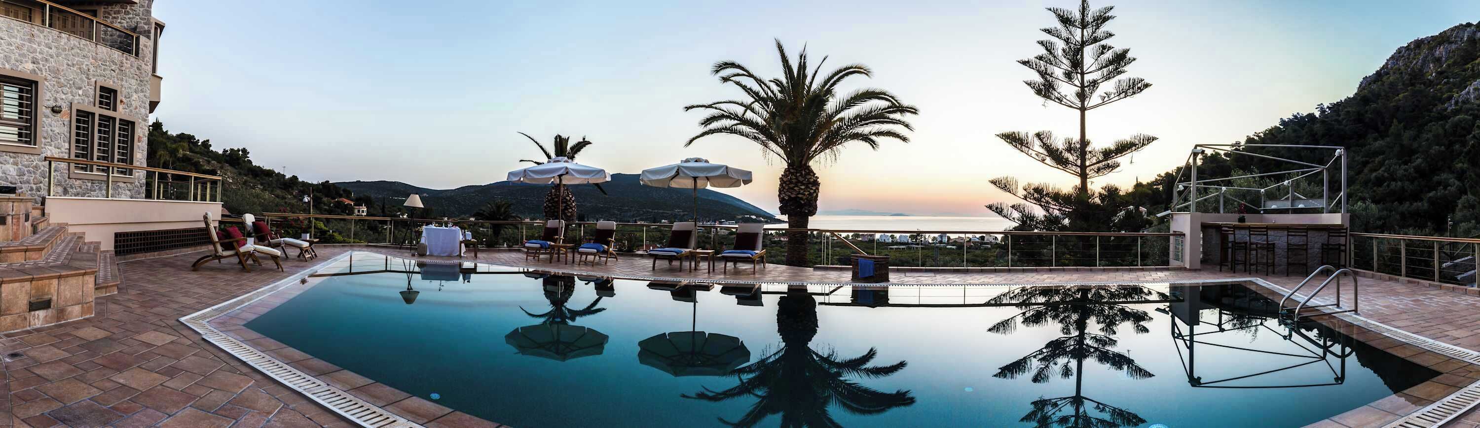 Zona de piscina con sillones de descanso, una palmera y vistas a la montaña.
