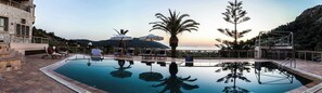 A pool area with lounge chairs, a palm tree, and a view of the mountains. - Epidavros Villas, Elia Garden Retreat, Shared Pool (Nea Epidavros)