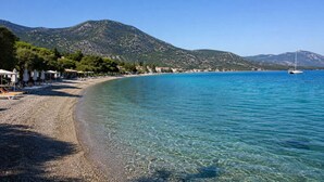 A beach with clear water, a boat, and mountains in the background. - Epidavros Villas, Elia Garden Retreat, Shared Pool (Nea Epidavros)