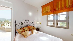 A bedroom with a bed, a window with curtains, a bedside table with a lamp, and a view of the outdoors. - Epidavros Villas, Elia Garden Retreat, Shared Pool (Nea Epidavros)