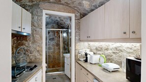 A compact kitchen with stone walls, a built-in shower, and modern appliances. - Epidavros Villas - Rodia Garden Retreat (Nea Epidavros)