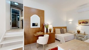 Habitación de hotel con cama, mesitas de noche, escritorio, silla, espejo y una escalera que lleva a otra habitación.