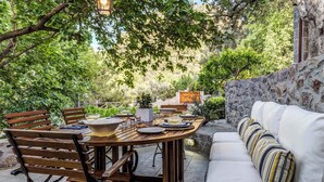 Un patio al aire libre con una mesa de madera lista para comer, rodeado por un muro de piedra y follaje.