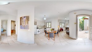 A spacious living area with a dining table, kitchen, and a large painting on the wall. - Epidavros Villas -  Dafni Stone & Garden Retreat (Nea Epidavros)
