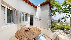 A wooden table with chairs and a white umbrella on a balcony overlooking a scenic view. - Epidavros Villas -  Dafni Stone & Garden Retreat (Nea Epidavros)