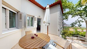 Taula de fusta amb cadires i un parasol blanc a un balcó amb vistes panoràmiques.
