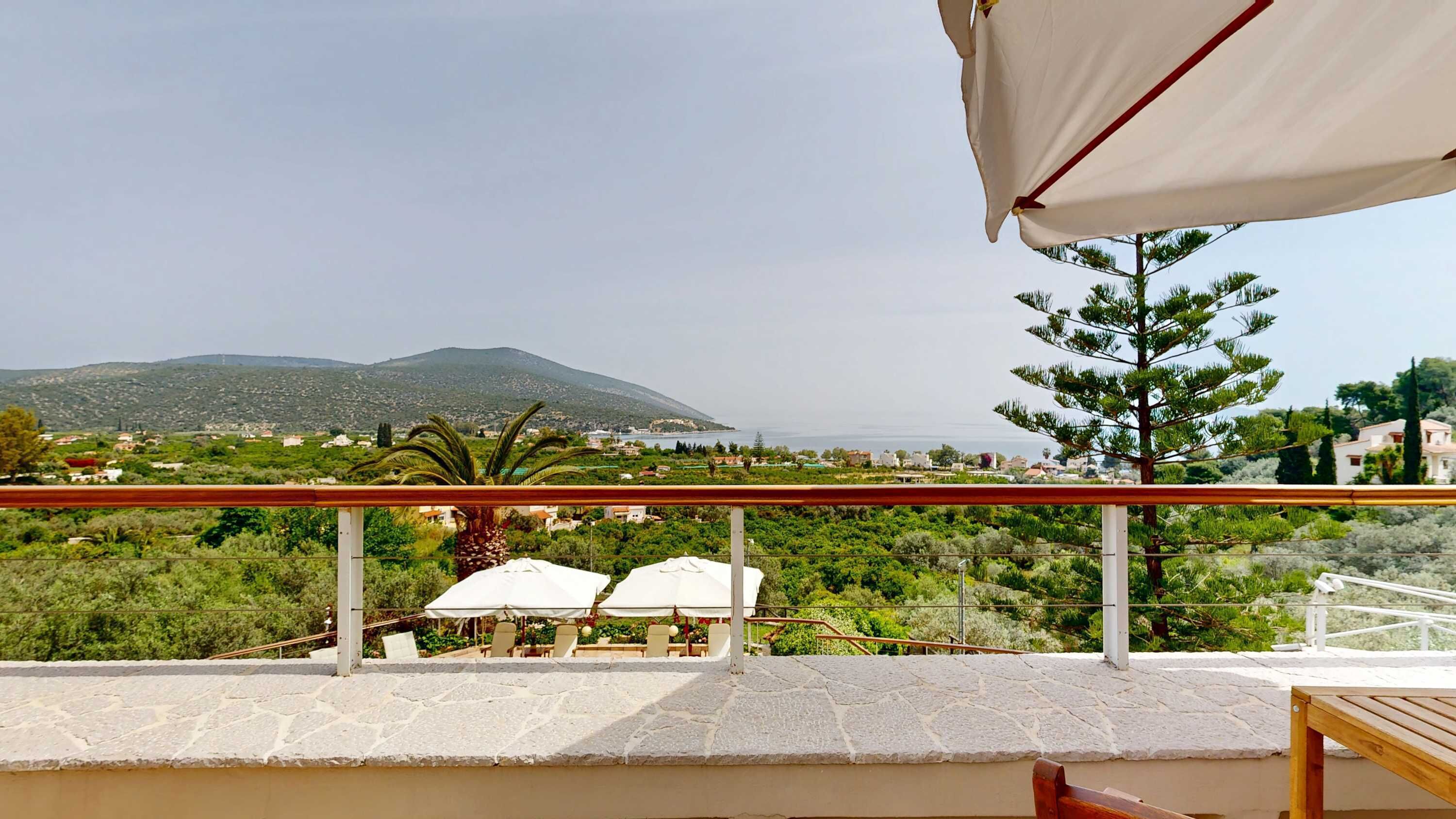 A terrace with stone flooring, outdoor seating, and a view of a coastal landscape with mountains.